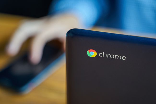 „Google Chromebook“ ant stalo šalia „Android“ telefoną naudojančio asmens
