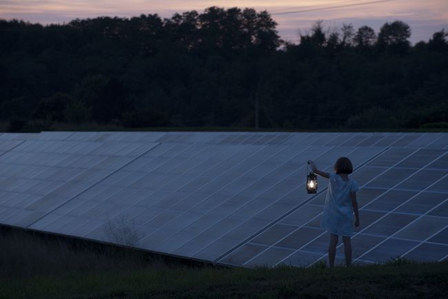 昔ながらのランタンを手に、夕暮れのソーラーパネルの前に立っている女の子