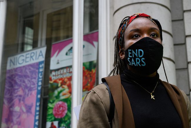 Een vrouw die een " END SARS" beschermend gezichtsmasker draagt, spreekt met de politie buiten het Nigeriaanse consulaat tijdens een demonstratie op 21 oktober 2020 in Londen, Engeland.