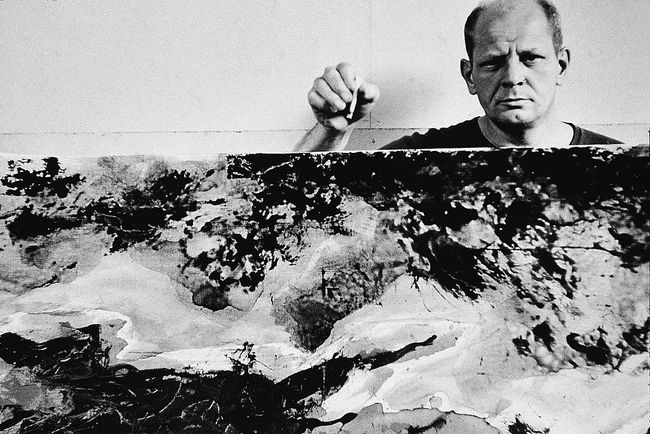 Americký abstraktní expresionistický malíř Jackson Pollock (1912 - 1956) drží cigaretu nad a za jedním ze svých obrazů ve svém ateliéru v 'The Springs,' East Hampton, New York, 23. srpna 1953.