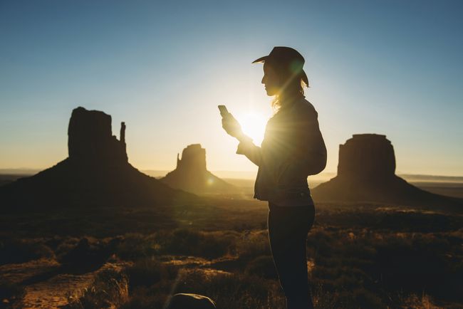 Nainen käyttää matkapuhelinta auringonnousun aikaan Monument Valleyssa