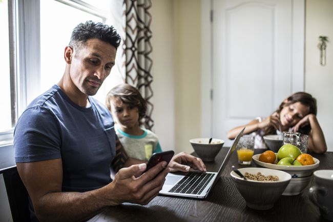 부모 앞에 노트북이 있는 아침 식탁에서 자녀의 휴대폰을 검토하는 부모.
