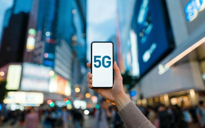 Някой държи смартфон в оживен град с изписано „5G“ на екрана.