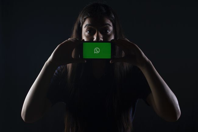 Ekranda WhatsApp logosu olan bir akıllı telefonu ağzının önünde tutan biri.