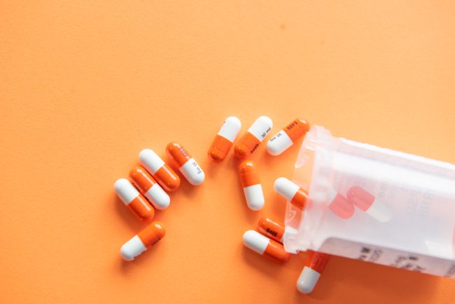 Narančaste i bijele tablete koje se izlivaju iz boce na narančastu pozadinu.