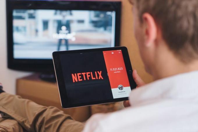 バックグラウンドでテレビをつけながらタブレットで Netflix を見ている人。 