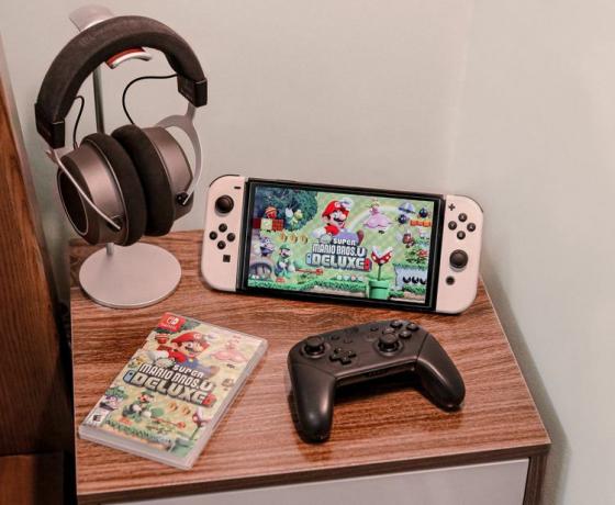 小さなテーブルの上に置かれた Nintendo Switch と、ヘッドセットとコントローラー、および「スーパー マリオ デラックス」ゲームの箱。