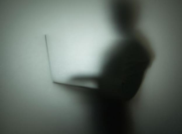 صورة ظلية لشخص يستخدم كمبيوتر محمول خلف زجاج