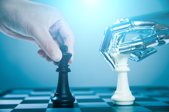Mão humana segurando uma peça de xadrez e a mão de metal Android segurando uma peça de xadrez representando o jogo de xadrez de computador