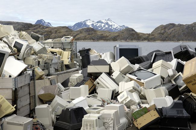 湖と山々を背景にした埋め立て地にある電子廃棄物（古いコンピューターと電子機器）の山。