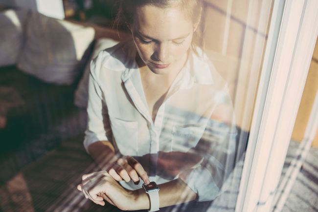 Frau am Fenster mit Blick auf Smartwatch