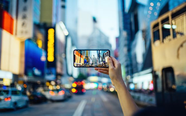 マルチカラーのネオンサインと都市交通の都市の高層ビルに対して忙しいダウンタウン地区でスマートフォンで写真を撮る人の手