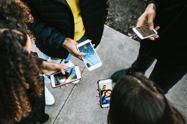 Bir grup genç yetişkin bir daire içinde duruyor ve hepsi akıllı telefonlarına bakıyor.