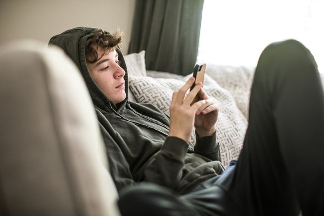 Um adolescente, recostado no sofá, usando um smartphone.