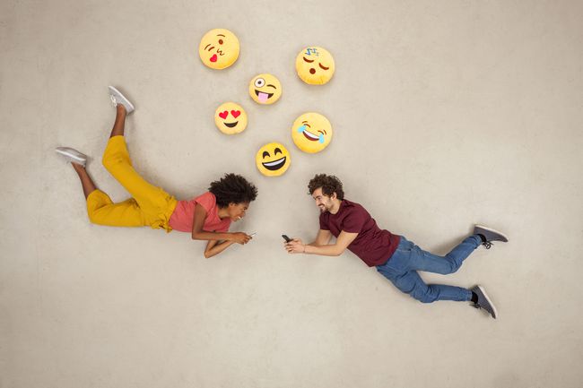 Lykkelige par sender tekstmeldinger på smarttelefonene sine og sender emojier