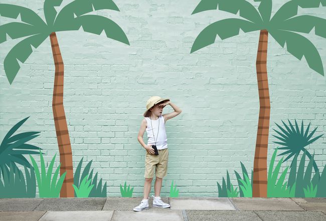 Un niño con un traje de safari de pie frente a una pintura de aventuras en la jungla.