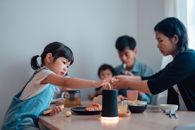 家族の夕食の席でスマートスピーカーと対話する幼い子供。