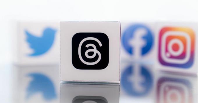 Threads logotipas priekiniame plane, o kiti socialinės žiniasklaidos logotipai fone nefokusuoti.