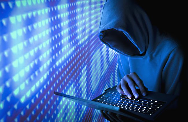 1과 0이 있는 파란색 벽 옆에 노트북을 들고 있는 얼굴 없는 컴퓨터 해커