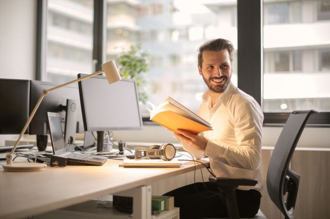 Homem com livro, laptop e monitor de desktop