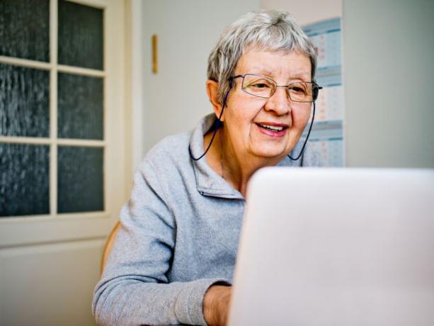 Starejša odrasla oseba doma uporablja prenosni računalnik. 
