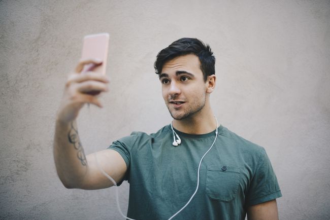 Mies puree huultaan ja ottaa selfietä kuulokkeet kaulassaan.