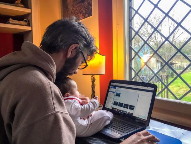집에서 노트북 작업을 하고 있는 한 남자가 아기를 안고 있습니다.