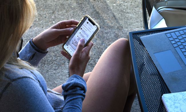 Moteris naudojasi išmaniuoju telefonu sėdėdama lauke
