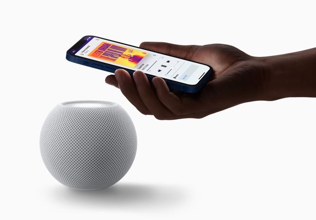 Крупный план руки, держащей смартфон над HomePod Mini.