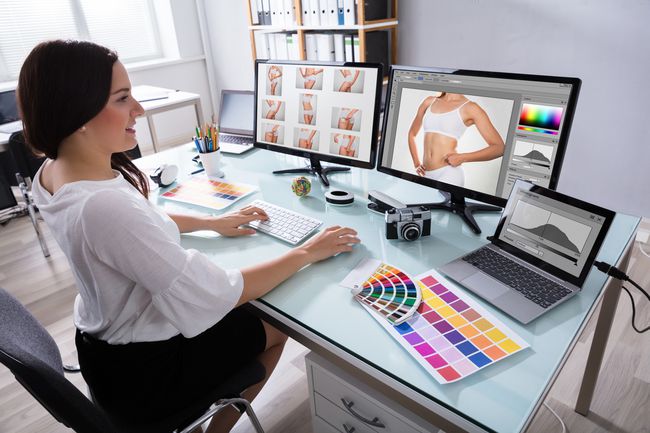 Iemand retoucheert foto's op twee computerschermen in een thuiskantoor.