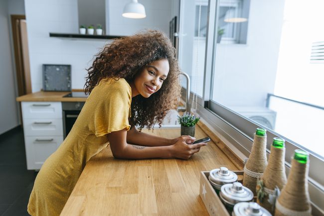 Nő használ mobiltelefont az otthoni konyhában
