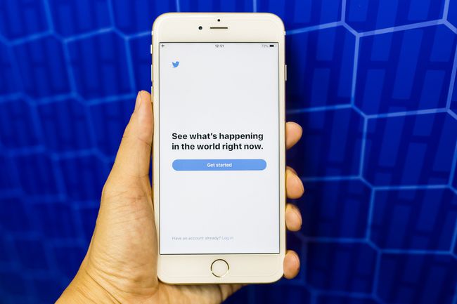 Uma mão segurando um iPhone mostrando a tela de introdução do Twitter, tudo contra um fundo azul brilhante.