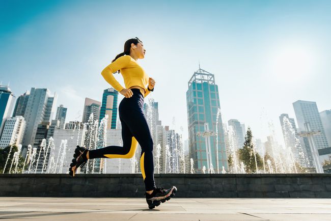 kvinde jogger, der løber i byparken i byen, med moderne byskyline som baggrund