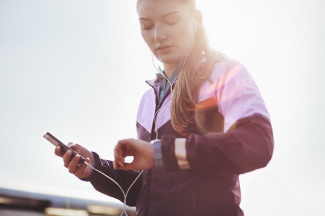 Un alergător care poartă căști verificând timpul pe smartwatch