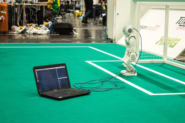 Bir robota bir kabloyla bağlı ekranda kod bulunan bir dizüstü bilgisayar. 