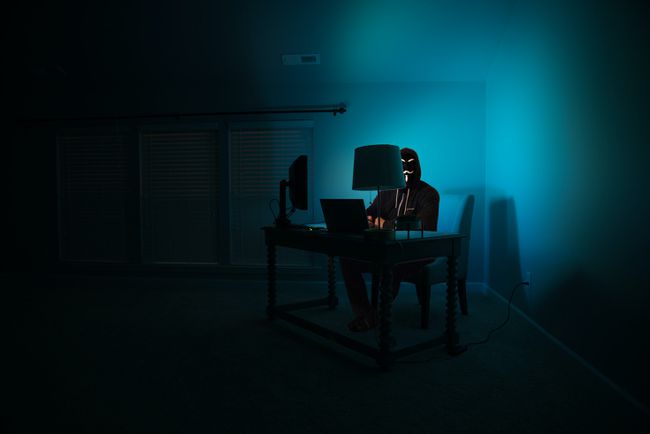 maskierter Mann, der mit einem Laptop im Dunkeln sitzt