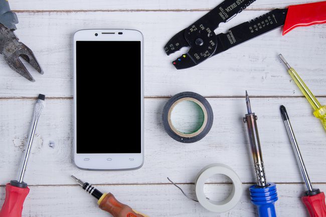 Поглед на паметни телефон одозго надоле окружен алатима који се користе за поправљање покварених телефона.