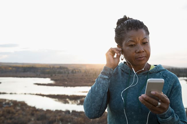 Moteris, kuri klausosi muzikos su ausinėmis ir žiūri į ežerą, bėgikė