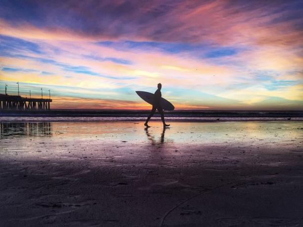 Homem com prancha de surf caminhando na praia