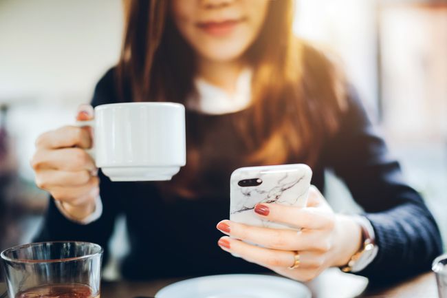 コーヒーを飲み、電話でメールをチェックする女性