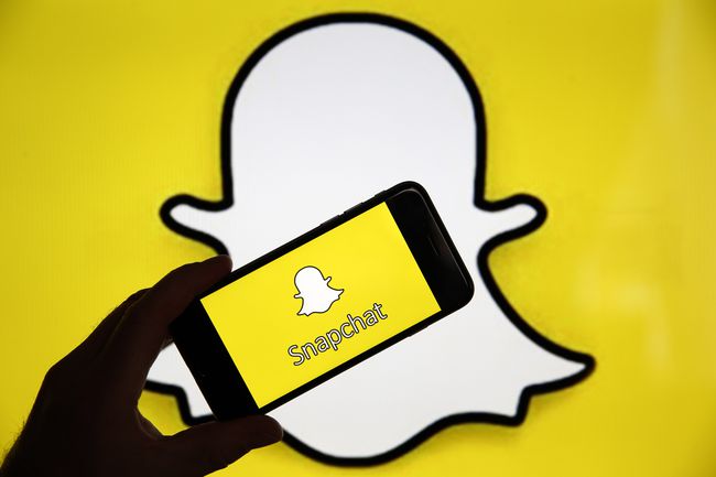 Snapchat logotips aiz rokas, kas tur Snapchat tālrunī