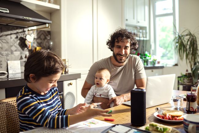 Sebuah keluarga duduk di meja dapur, dengan speaker pintar di tengah meja.
