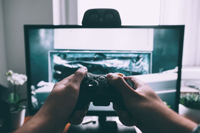 Mãos segurando um controlador de jogos na frente de um monitor