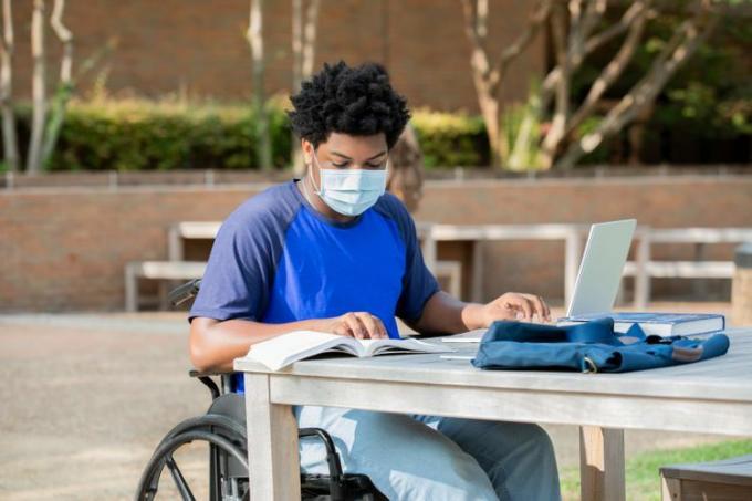 Um estudante estudando ao ar livre com um laptop e um livro