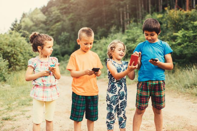 屋外でスマートフォンを使用している4人の子供。