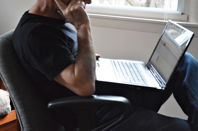 Un bărbat care folosește un laptop cu Windows lângă o fereastră.