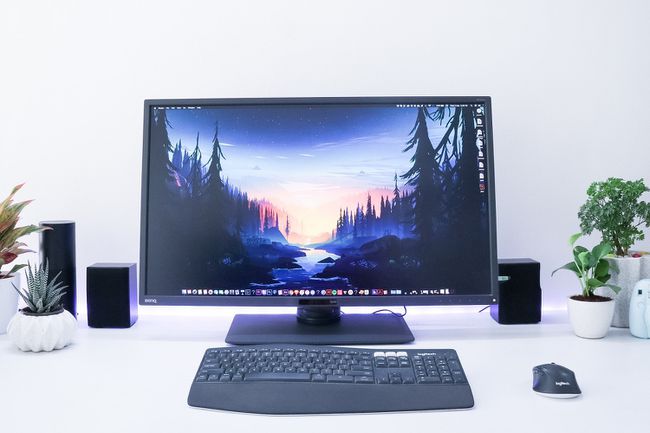 Beyaz bir duvarın önünde beyaz bir masada siyah PC monitörü, klavye ve fare.