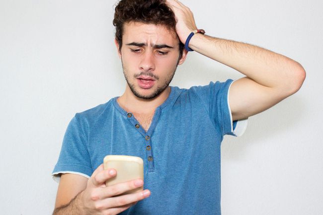 Молодой человек в синей футболке грустит из-за того, что его заблокировали в мобильном приложении Facebook