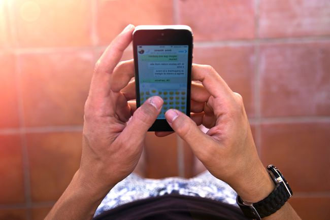 Vaikinas rašo žinutes su išmaniuoju telefonu siunčiančiomis šypsenėlėmis