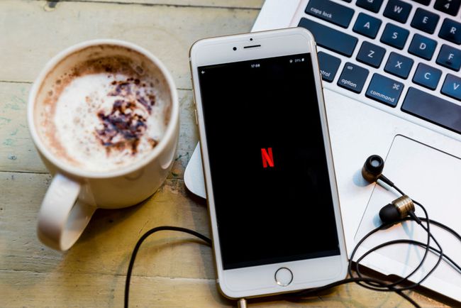 logo Netflix zobrazené na smartphonu, který sedí na notebooku s šálkem kávy poblíž.